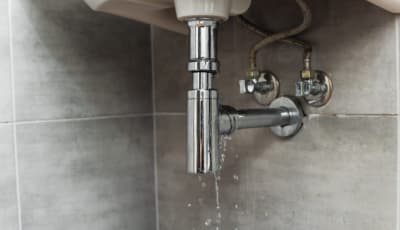 Leaking pipe under a bathroom basin with water dripping onto tiles in Brisbane